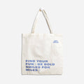A white tote bag with blue text. The text reads "FIND YOUR FUN & BE BOLD SMILES FOR MILES" with a smiley face symbol between each phrase. The bottom right corner displays the text "epic blend."
