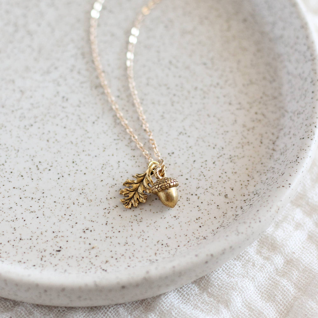 Gold necklace with acorn pendant on a textured white surface