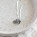 Silver necklace with acorn and leaf charm on a textured white surface