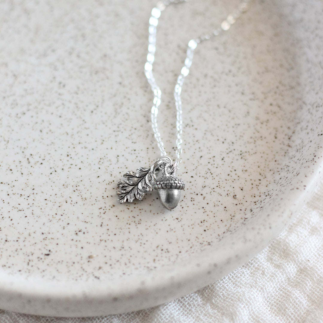 Silver necklace with acorn and leaf charm on a textured white surface