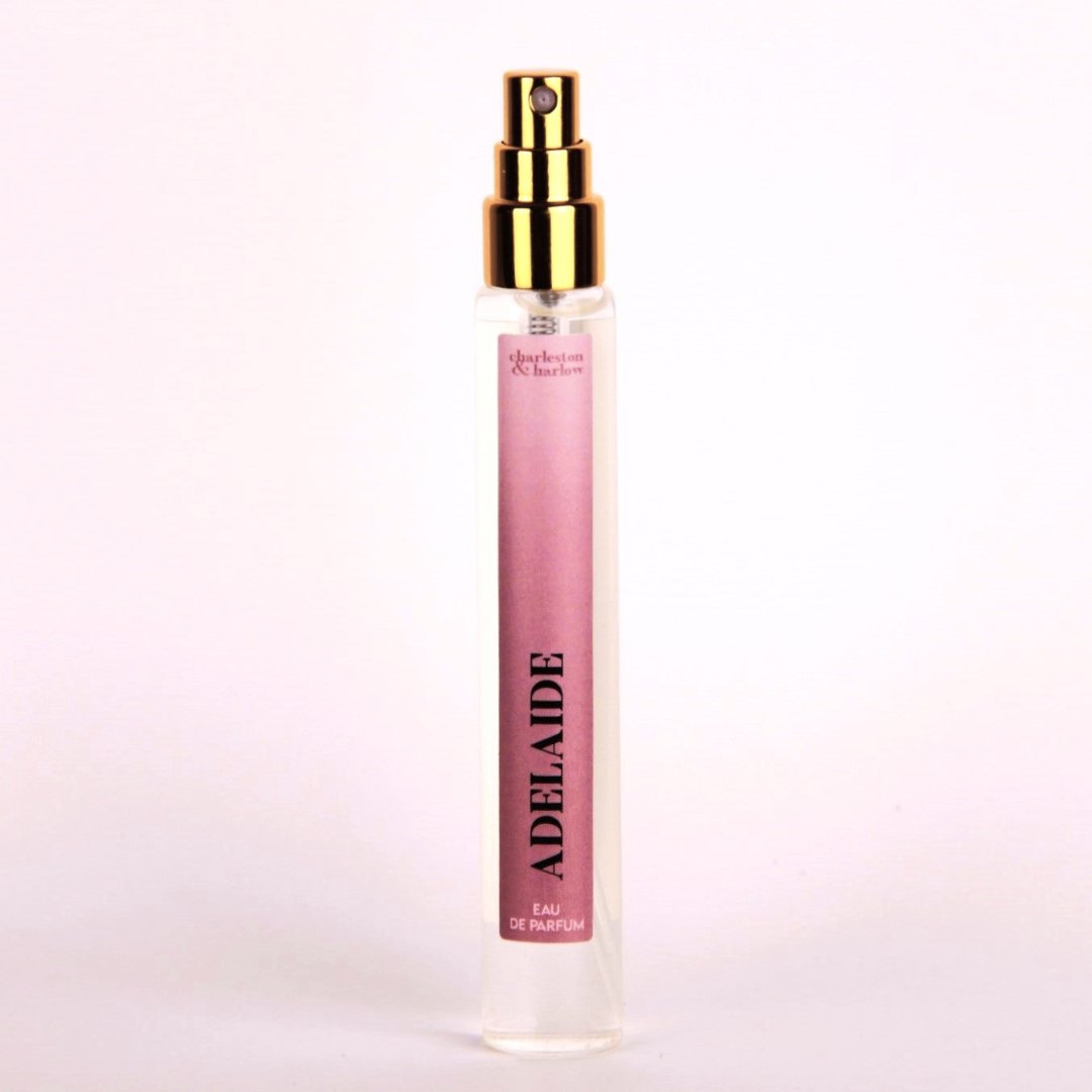 A small, clear glass perfume bottle with a gold cap and sprayer. The label reads "ADELAIDE" in pink letters and "EAU DE PARFUM" in smaller black letters. The background is white.