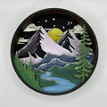 A Paint By Layers Craft Kit featuring a circular shadow box with a pre-designed landscape scene. The scene depicts a mountain range under a starry night sky, with a river flowing through a valley. The kit includes layers of wood, paint, and instructions. The title of the kit is "Adventure Awaits Shadow Box."