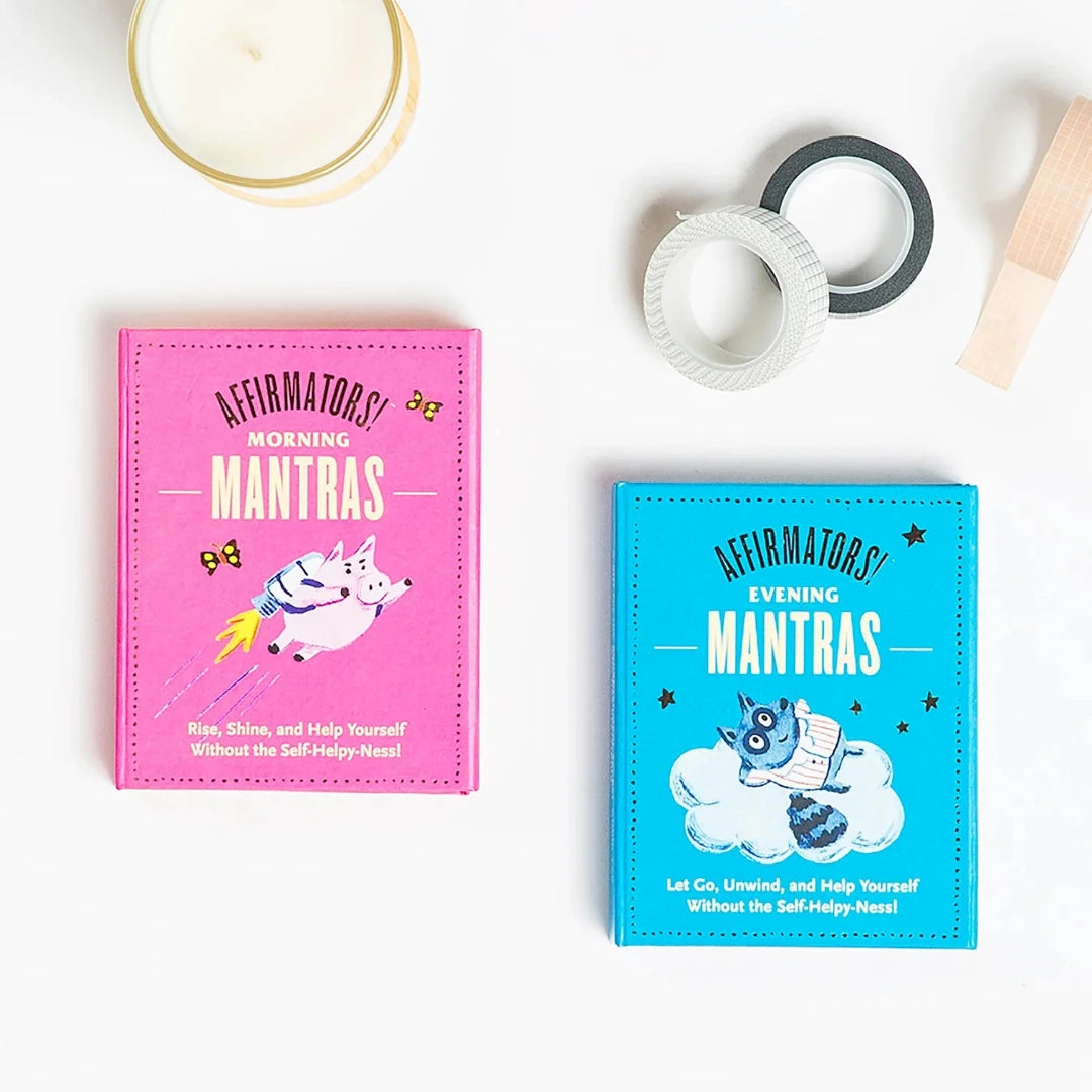 A pink box containing a deck of affirmation cards. The box has the text "AFFIRMATORS! EVENING MANTRAS" on the front. The cards have various affirmations printed on them, including "Let Go, Unwind, and Help Yourself Without the Self-Helpy-Ness!" and "Thank you to me! For always being willing to try, what's next." The box also includes a small booklet with additional affirmations.