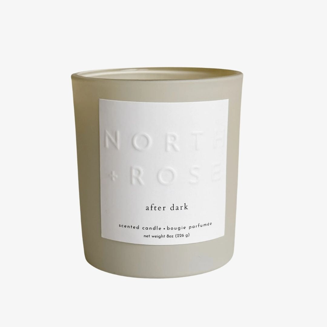 A frosted glass scented candle in a light beige-gray color with a large white label that reads 'NORTH + ROSE after dark'.