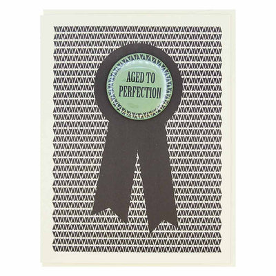 A birthday card with a black and white geometric pattern in the background. A large black ribbon graphic is overlaid, and centered on it is a round, mint green button with a white scalloped edge. The button reads 