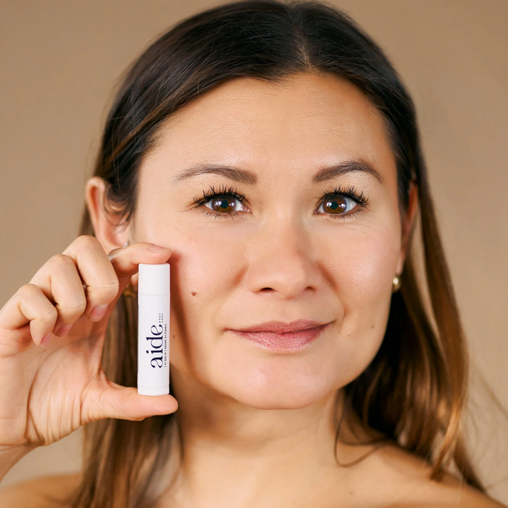 A person holding a  white tube of lip balm with the word 