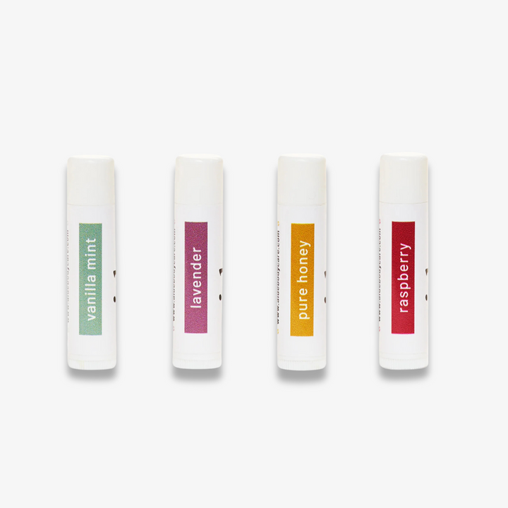 Four lip balms lined up in a row from left to right: vanilla mint, lavender, pure honey, and raspberry.