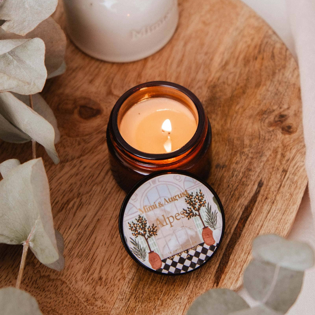 Candle in a decorative container on a wooden surface with eucalyptus leaves.