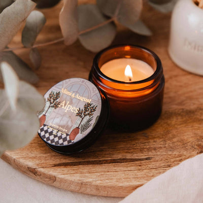 Candle in a glass jar with a decorative label on a wooden surface, surrounded by eucalyptus leaves.