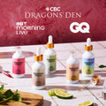 Five Shroom Soda dropper bottles in assorted pastel colors are arranged on a tiled surface with lime slices, mint, and a glass dropper nearby. The background is a textured dusty pink wall with CBC Dragons' Den, GTV Morning Live, and GQ logos at the top.