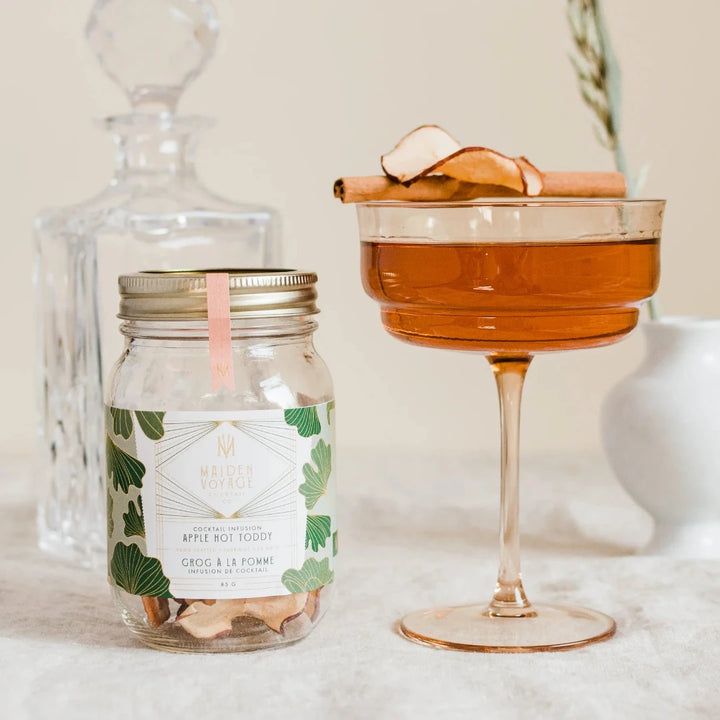 A glass jar filled with dried apple slices, cinnamon sticks, and star anise. The jar has a white label with the Maiden Voyage logo and the product name 