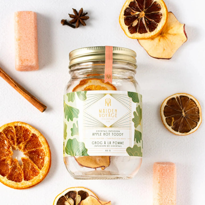 A glass jar filled with dried apple slices, cinnamon sticks, and star anise. The jar has a white label with the Maiden Voyage logo and the product name 
