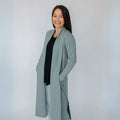 Woman wearing a long light blue coat over a black top against a white background