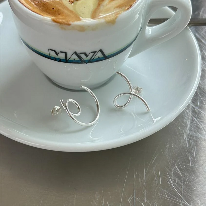 A pair of asymmetric twist earrings made of sterling silver, featuring a unique, abstract, and mismatched swirling design, displayed on a white plate. These modern earrings are available in Ottawa, Ontario, Canada