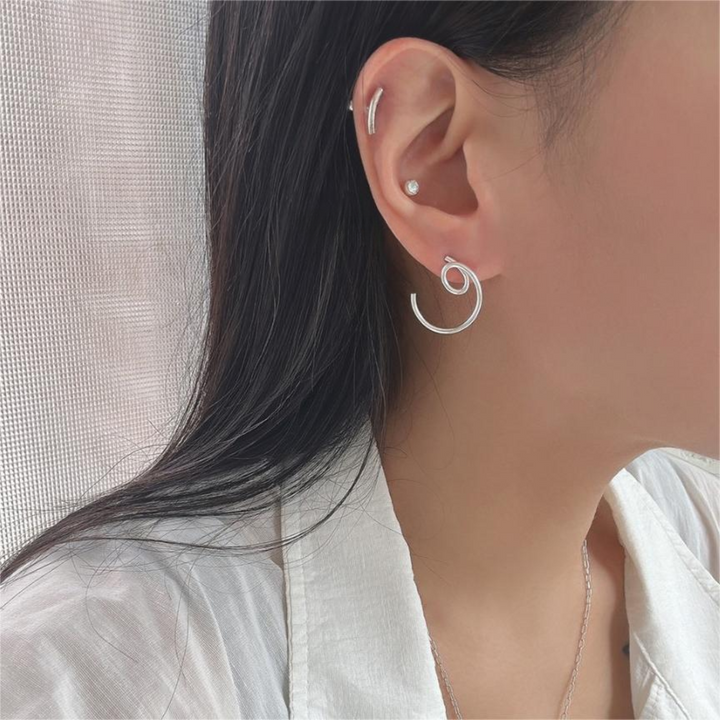 A pair of asymmetric twist earrings made of sterling silver, featuring a unique, abstract, and mismatched swirling design, displayed on a white plate. These modern earrings are available in Ottawa, Ontario, Canada