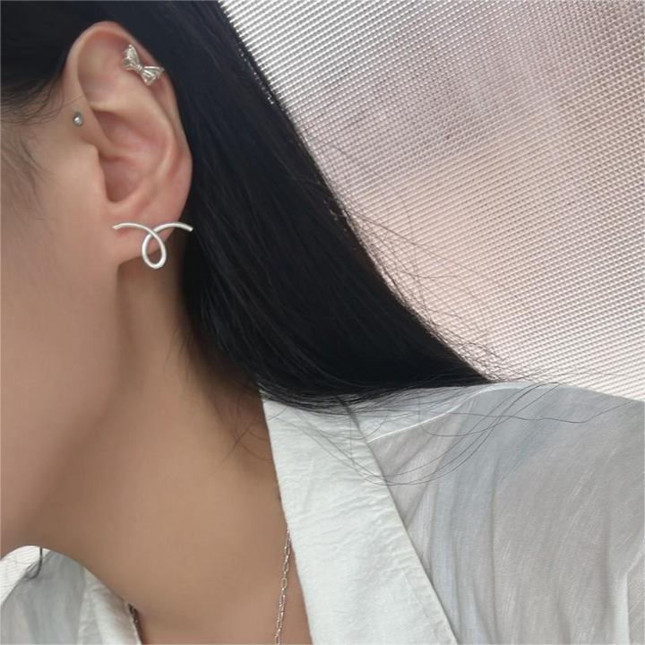 A pair of asymmetric twist earrings made of sterling silver, featuring a unique, abstract, and mismatched swirling design, displayed on a white plate. These modern earrings are available in Ottawa, Ontario, Canada