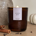Candle labeled 'autumn spice' with cinnamon sticks and cloves on a wooden surface