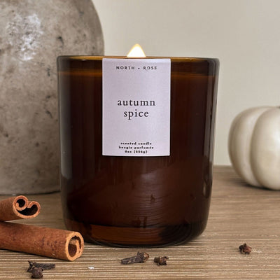 Candle labeled 'autumn spice' with cinnamon sticks and cloves on a wooden surface