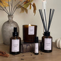 Autumn-themed diffusers, candles, and bottles on a wooden surface with decorative leaves and pumpkins.