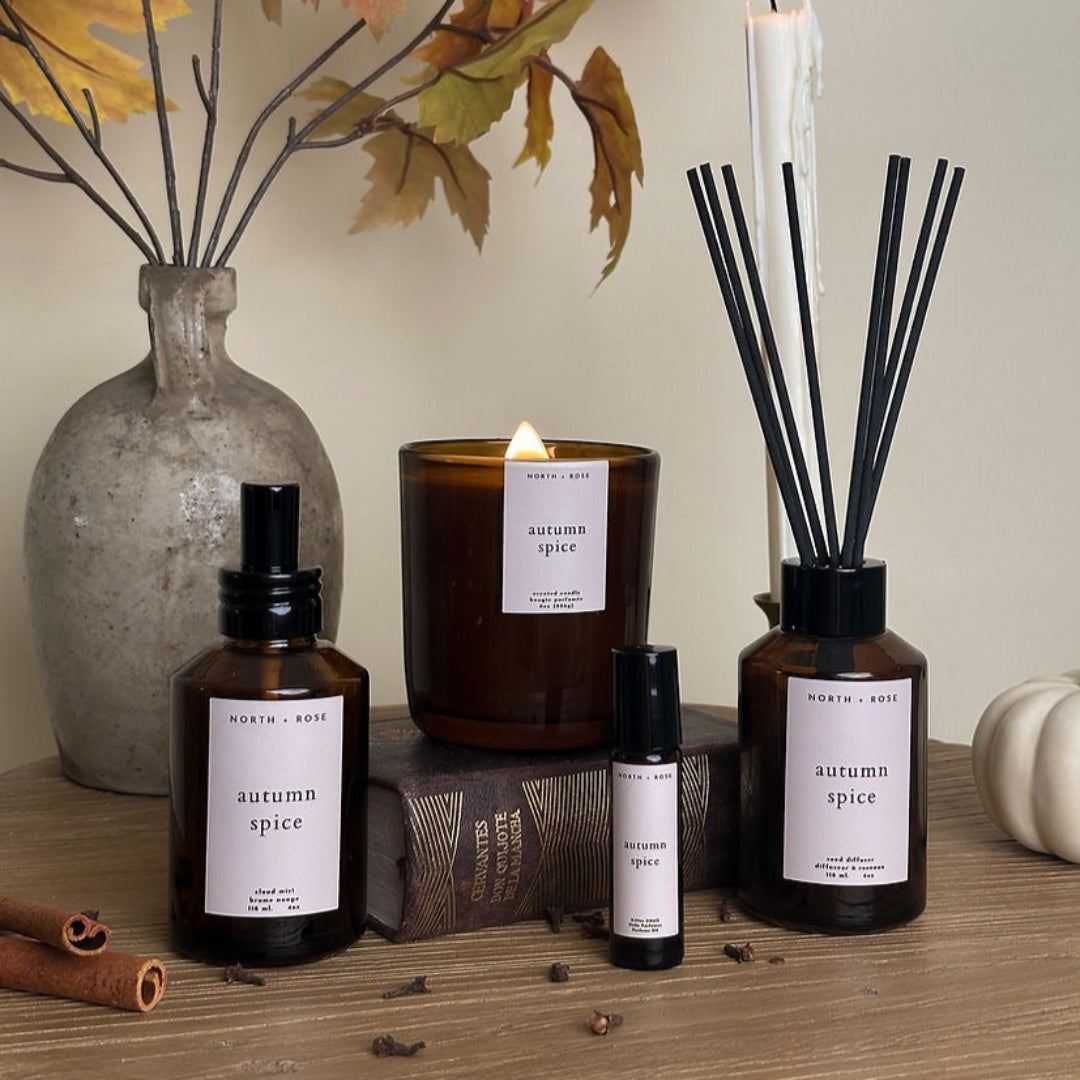 Autumn-themed diffusers, candles, and bottles on a wooden surface with decorative leaves and pumpkins.