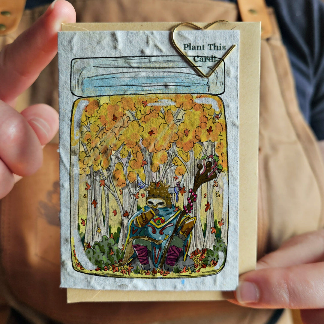 Card with a design of a forest scene with a character holding a seedling, held by a person.