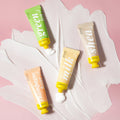 Three tubes of hand cream with visible brand names on a pink background
