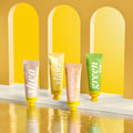 Four colorful tubes of hand lotion on a reflective surface with a yellow and beige archway background.