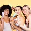 Three women holding skincare products against a yellow background