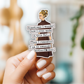 Hand holding a sticker with text and a woman's face, blurred background