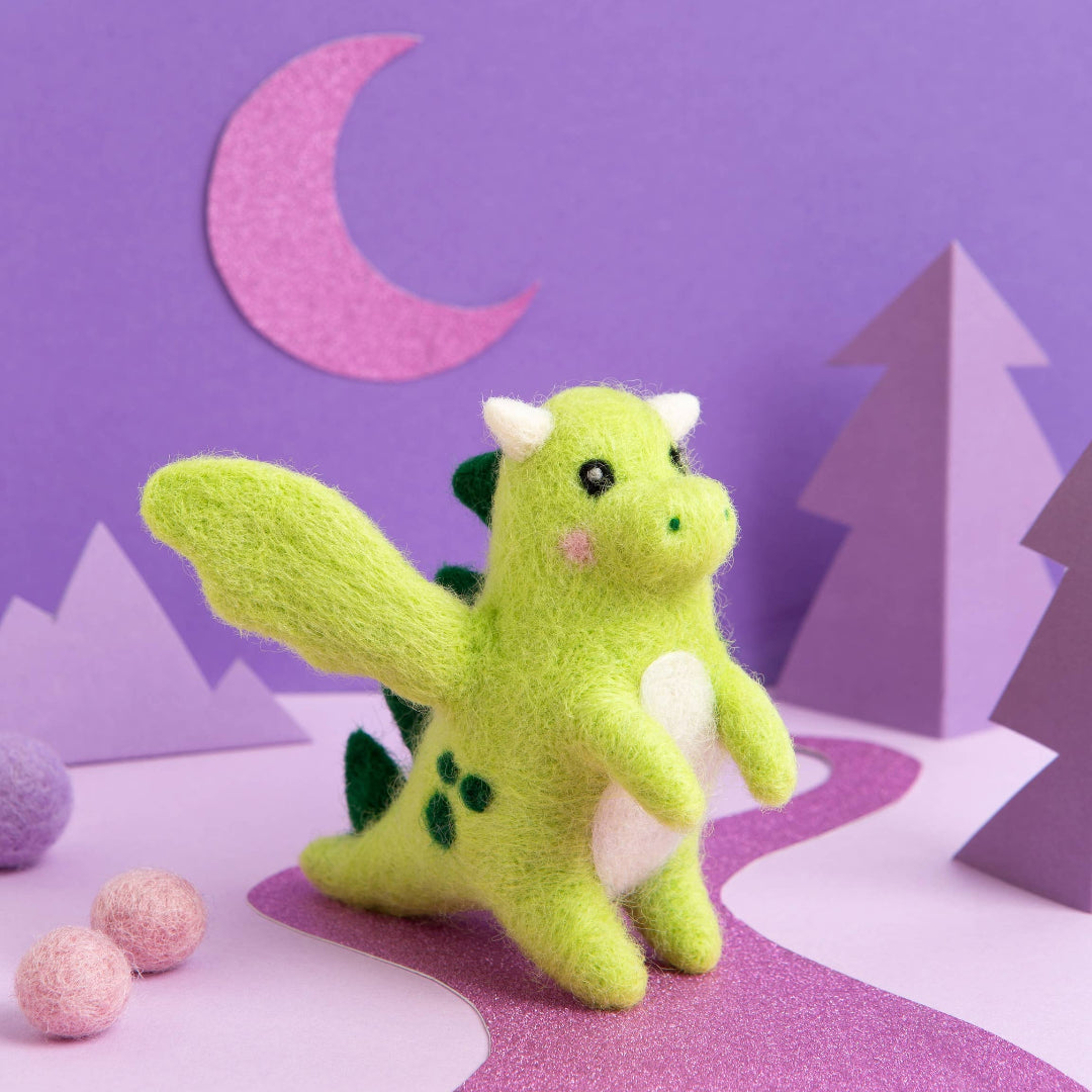 Green plush dragon toy on a purple landscape with trees and moon