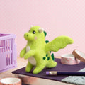 Green plush dragon toy on a pink surface with stationery items.