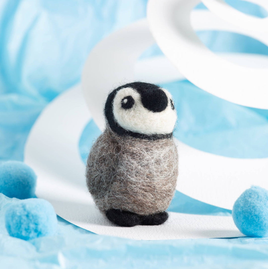 Felted penguin toy on a white base with a blue and white background