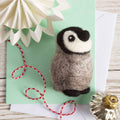Felted penguin toy on a green card with decorative elements on a wooden surface