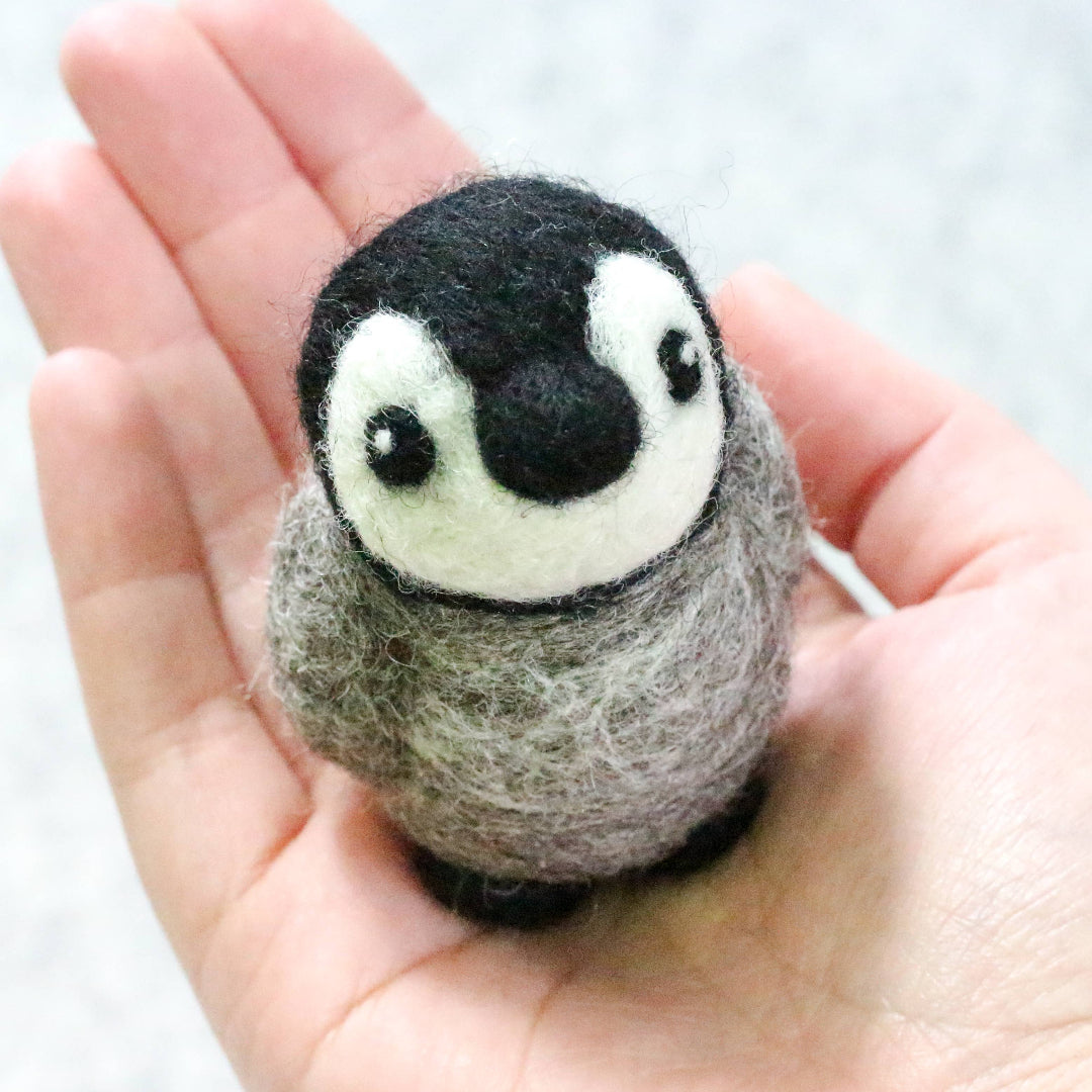 Felted penguin toy held in a hand against a white background
