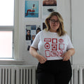 Person wearing a white t-shirt with red graphics in a room with white walls and a radiator.