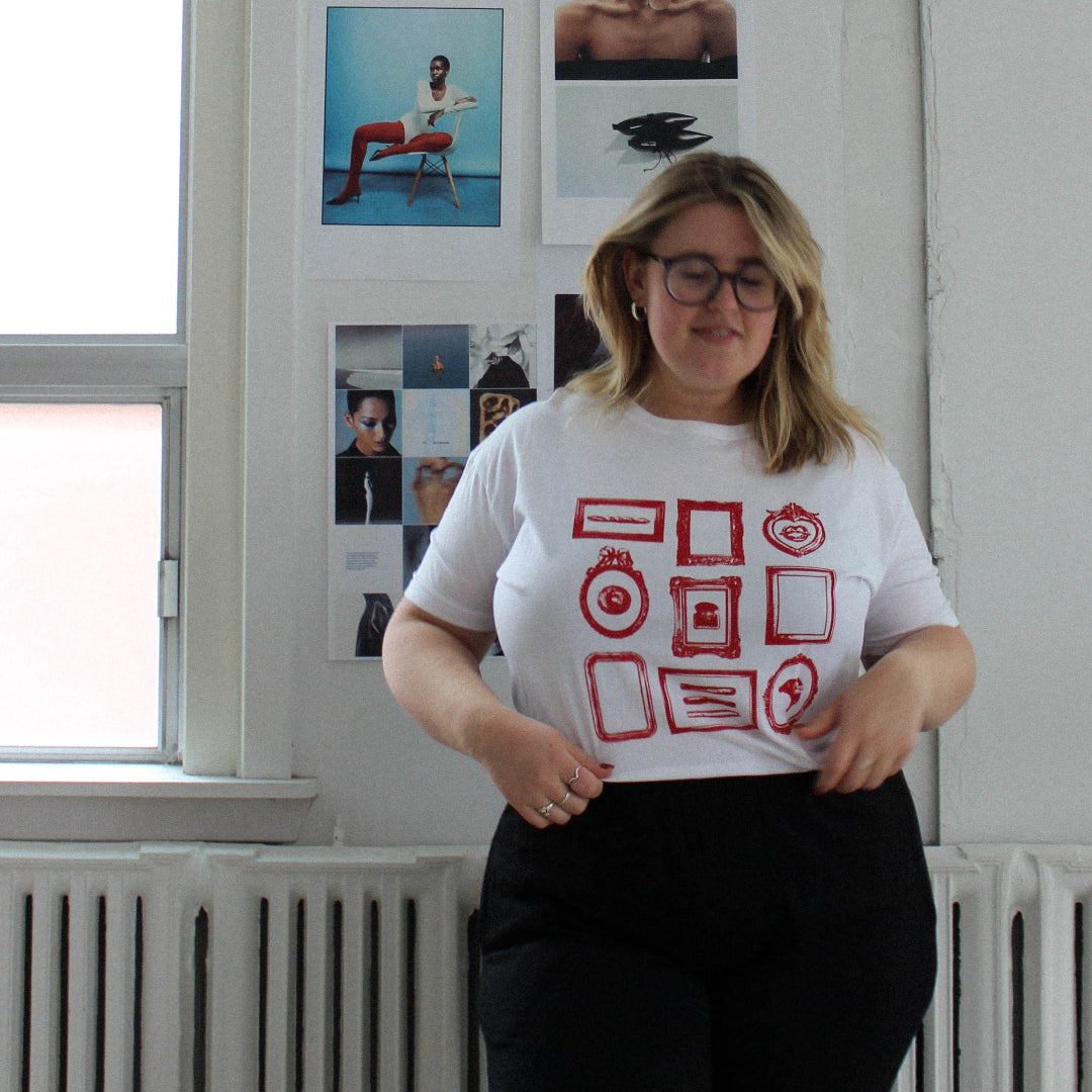 Person wearing a white t-shirt with red graphics in a room with white walls and a radiator.