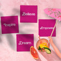 Pink napkins with motivational words on a pink surface with a drink and fruit.