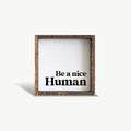 Wooden-framed sign with 'Be a nice Human' text on a white background