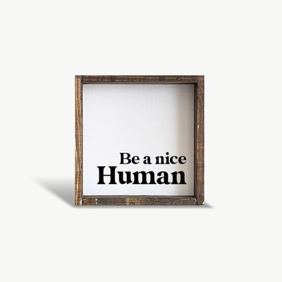 Wooden-framed sign with 'Be a nice Human' text on a white background