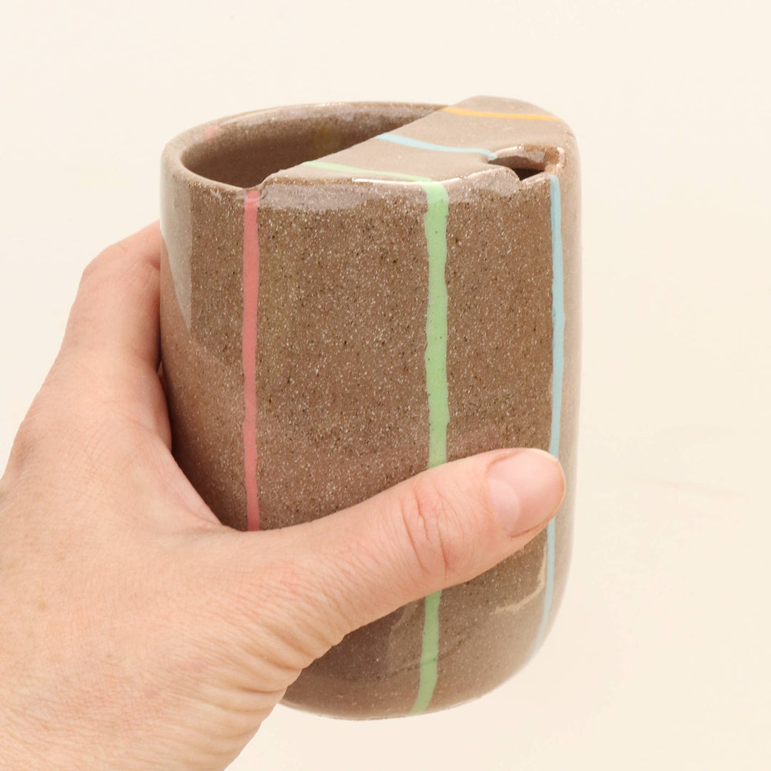 Hand holding a ceramic cup with striped design on a beige background