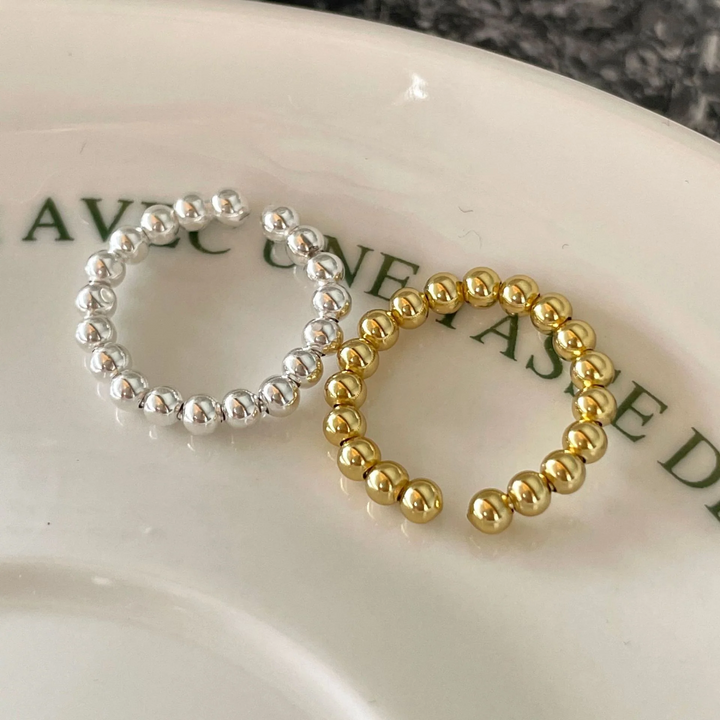 A set of silver and gold bead rings, each with a delicate design of small spheres and an adjustable, open band, displayed on a patterned ceramic surface. These dainty and stackable rings are available in Ottawa, Ontario, Canada.