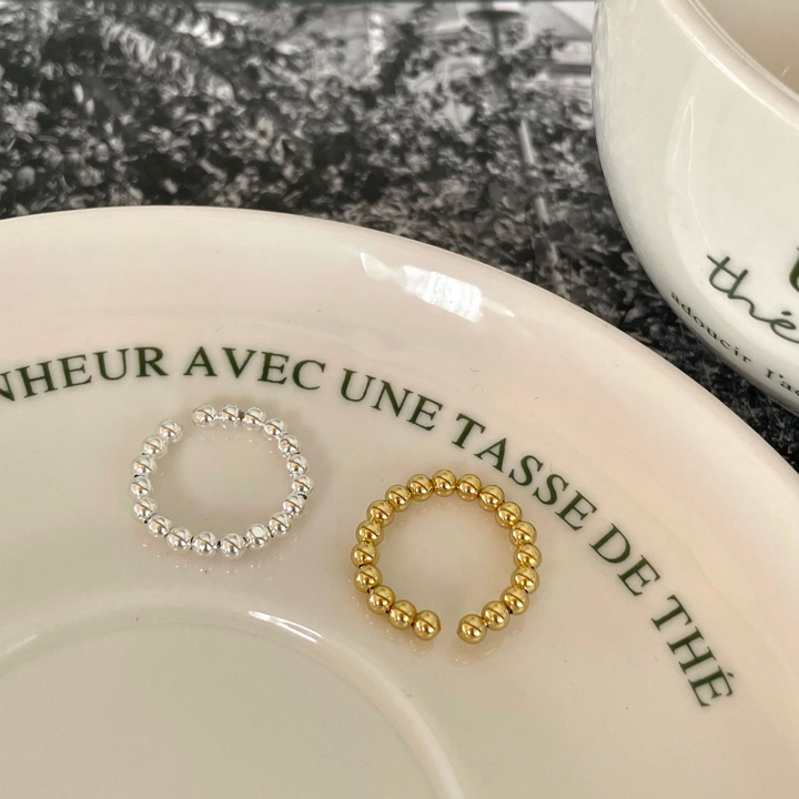 A set of silver and gold bead rings, each with a delicate design of small spheres and an adjustable, open band, displayed on a patterned ceramic surface. These dainty and stackable rings are available in Ottawa, Ontario, Canada.