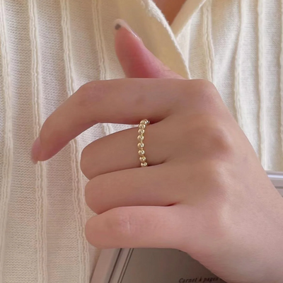 An 18K gold plated bead ring with a delicate design of small spheres, worn on a person's finger. This adjustable and stackable ring is available in Ottawa, Ontario, Canada.