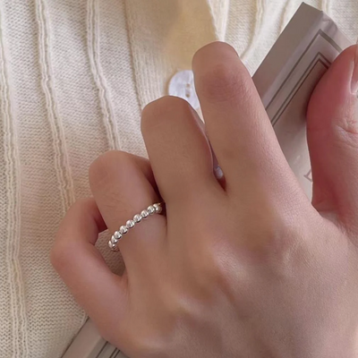 A silver bead ring with a delicate design of small spheres, worn on a person's finger. This adjustable and stackable ring is available in Ottawa, Ontario, Canada.