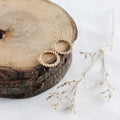 Gold hoop earrings on a wooden surface with dried branches.