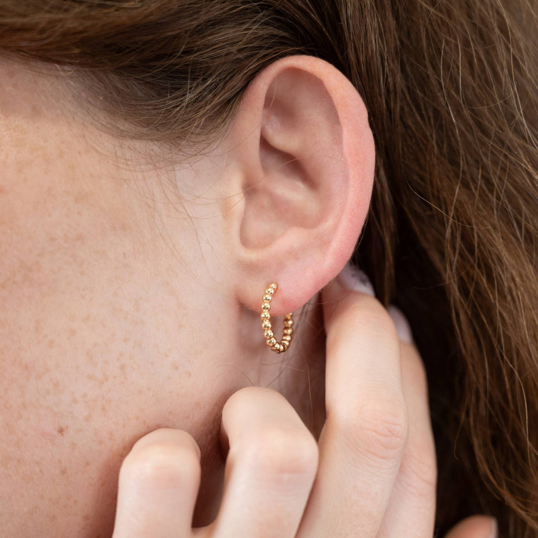 Close-up of a person wearing a gold hoop earring with a hand adjusting it.