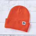 Orange beanie with a small logo on a light wooden surface