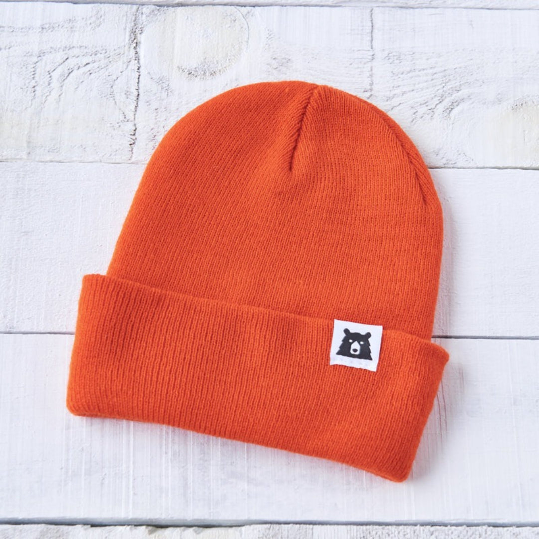 Orange beanie with a small logo on a light wooden surface