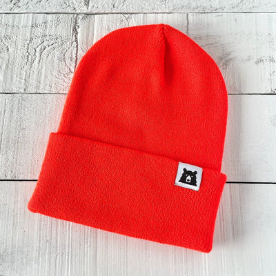 Red beanie with a small logo on a light wooden surface