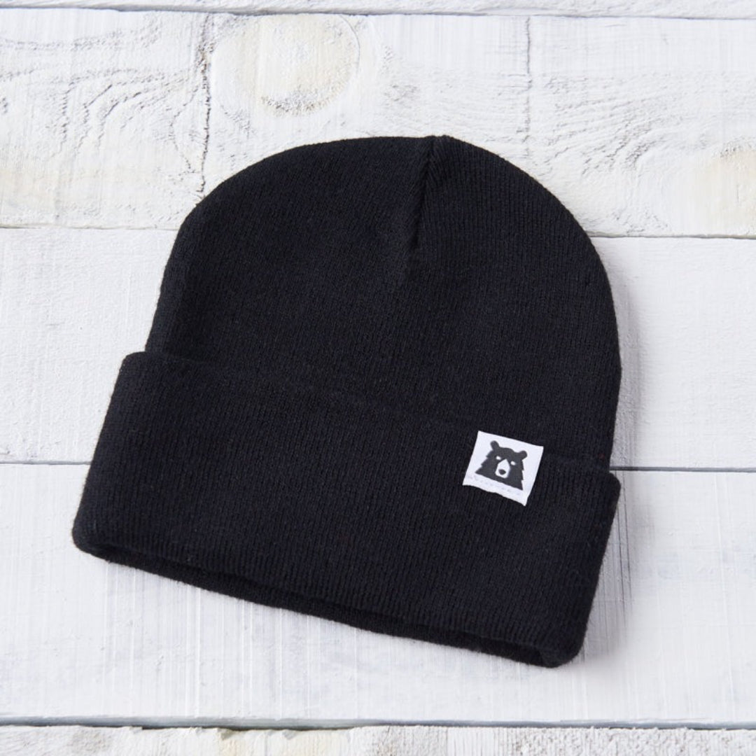 Black beanie with a logo on a light wooden surface